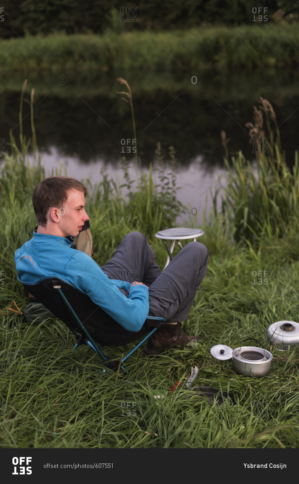 Teen man sitting at waterfront with camping stove