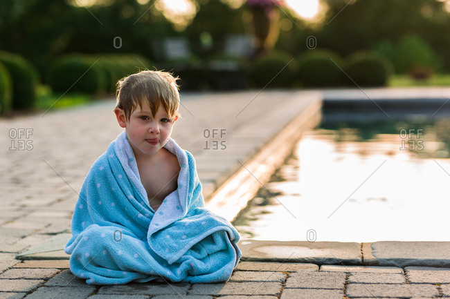 Young boy wrapped in towel sitting by pool