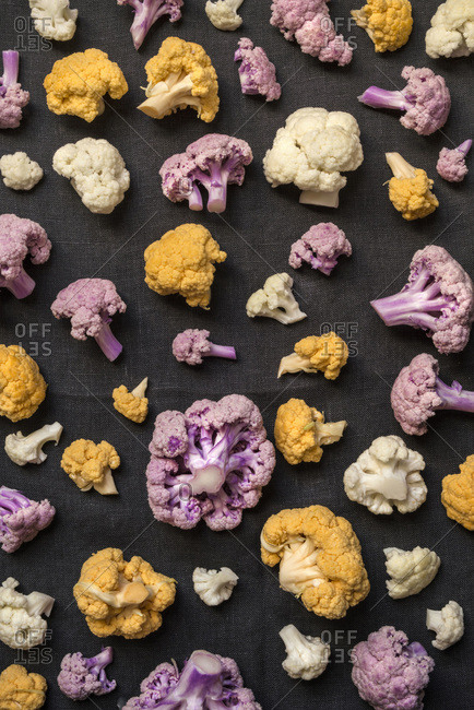 An array of gold, pink and white cauliflower scattered on a dark gray linen