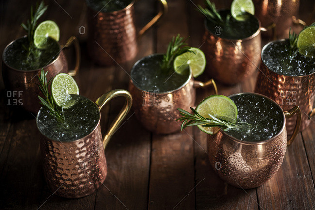 Multiple moscow mule drinks in copper mugs on rustic wood surface with rosemary and lime garnishes