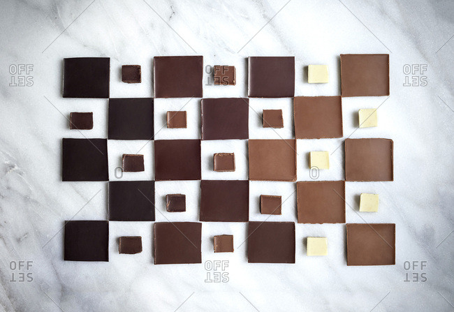 A geometric layout of chocolate squares in ombre pattern from dark chocolate to white chocolate on a marble surface