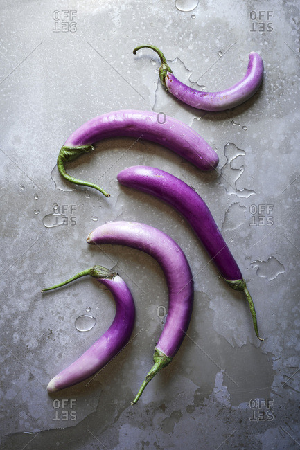 A layout of rich, purple, Asian eggplants with water on a textured wooden surface