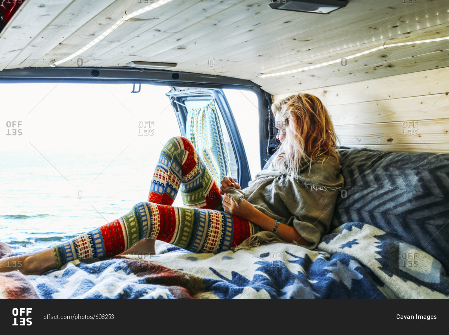 Woman looking at sea while leaning on mattress in travel trailer