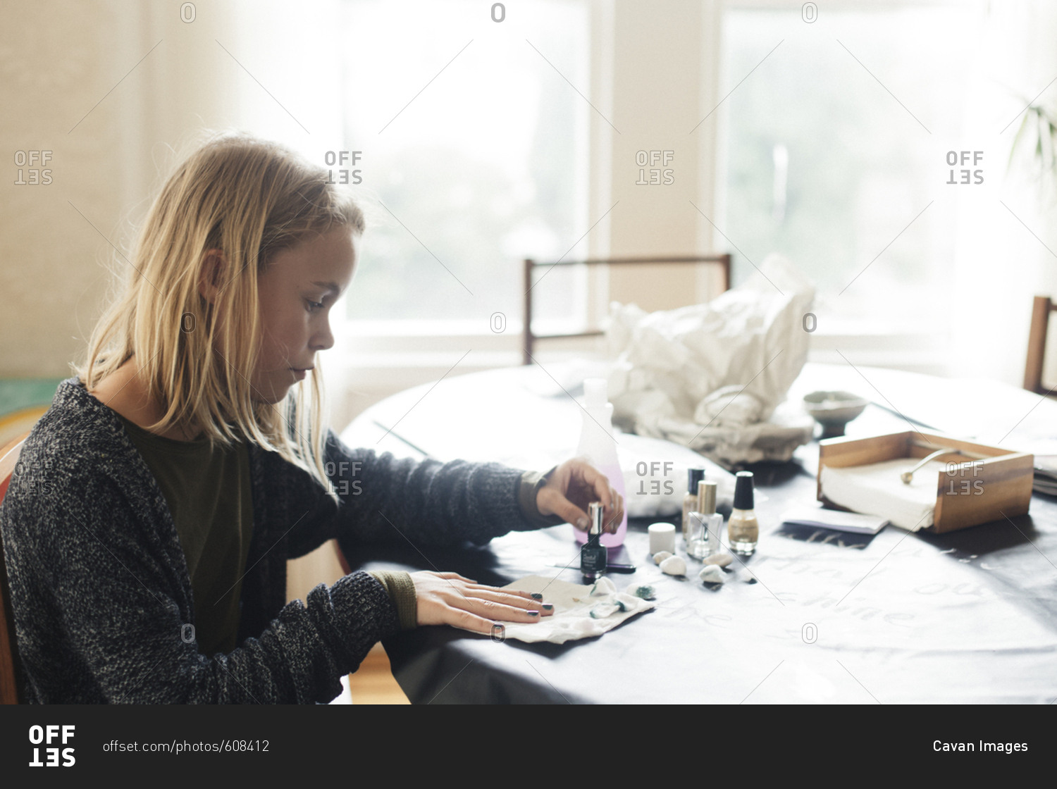 Girl painting fingernails on table while sitting against window