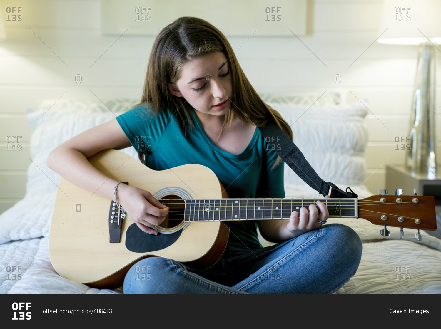 Teenage girl plucking guitar in bedroom