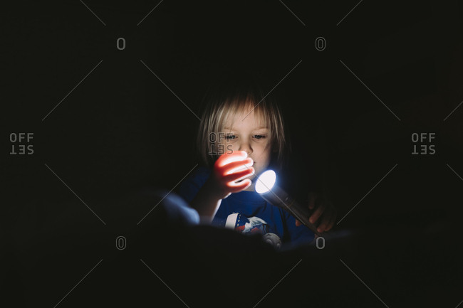 Boy playing with flashlight in darkroom
