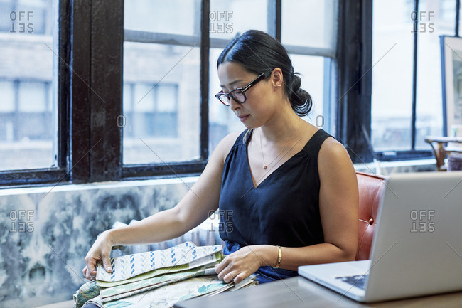 Interior designer looking at curtain samples while sitting against windows in workshop