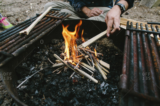 Cropped Hand Of Man Burning Firewood In Fire Pit At Campsite Stock