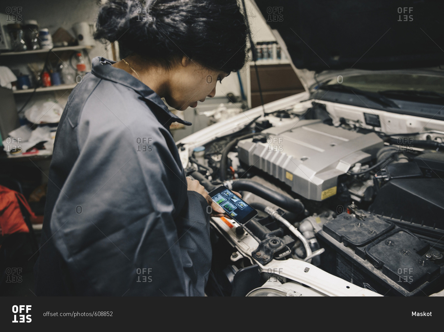 Female mechanic using application on smart phone while standing by open car hood