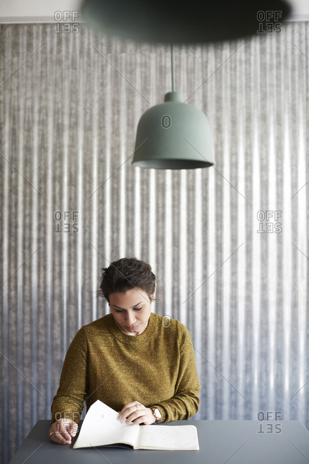 Businesswoman reading document while sitting at desk against corrugated iron wall in creative office