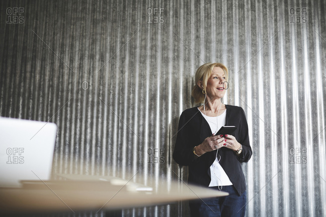 Smiling senior businesswoman talking on mobile phone against corrugated iron wall at creative office