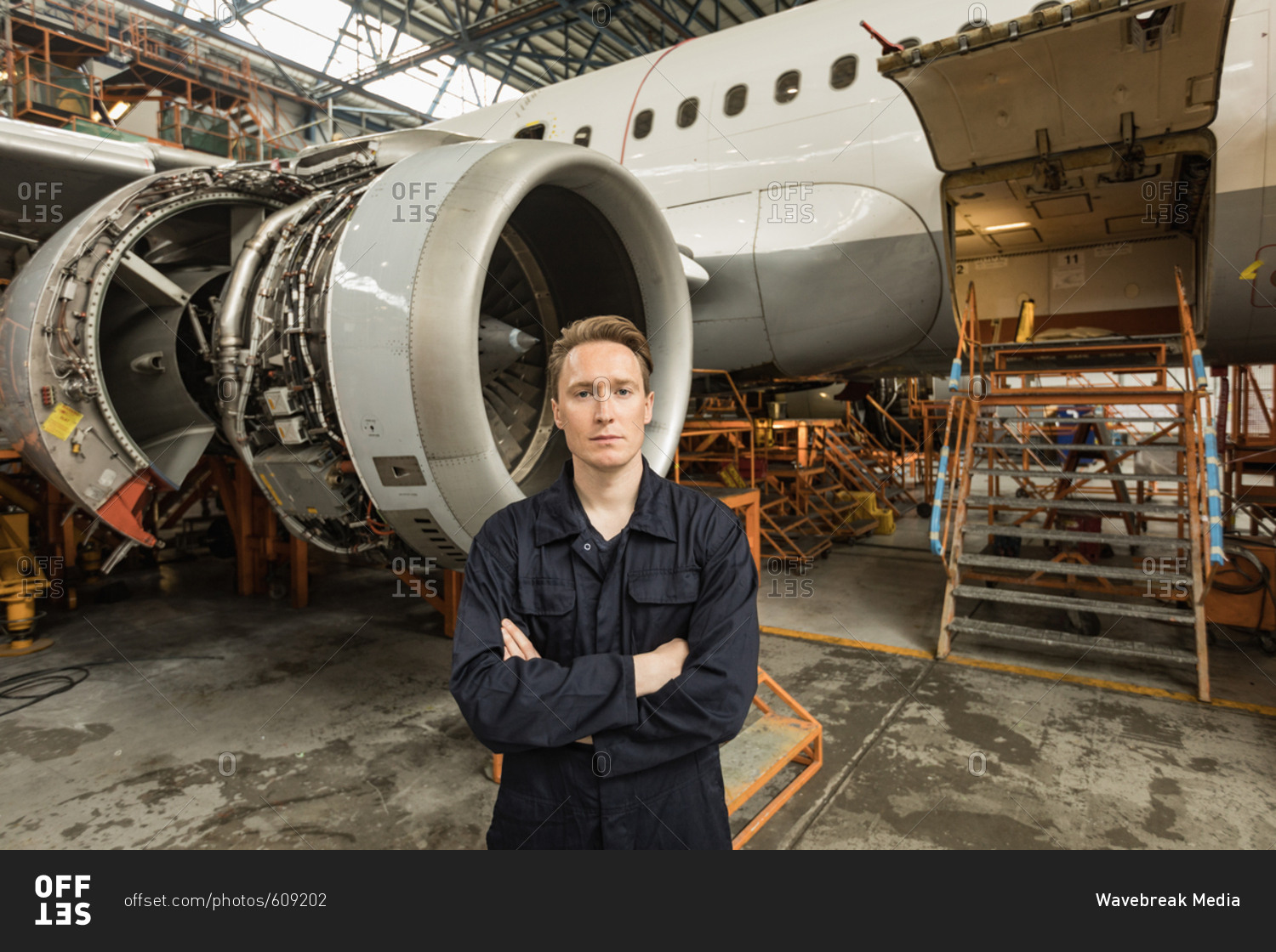 Portrait of male aircraft maintenance engineer standing with arms crossed at airlines maintenance facility