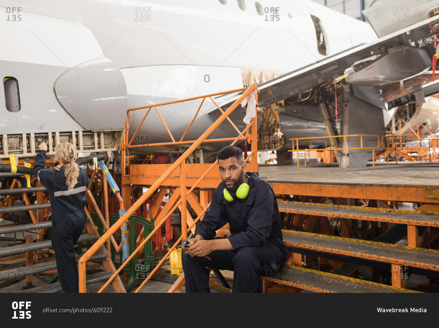 Female aircraft maintenance engineers working over an aircraft while colleague relaxing at airlines maintenance facility