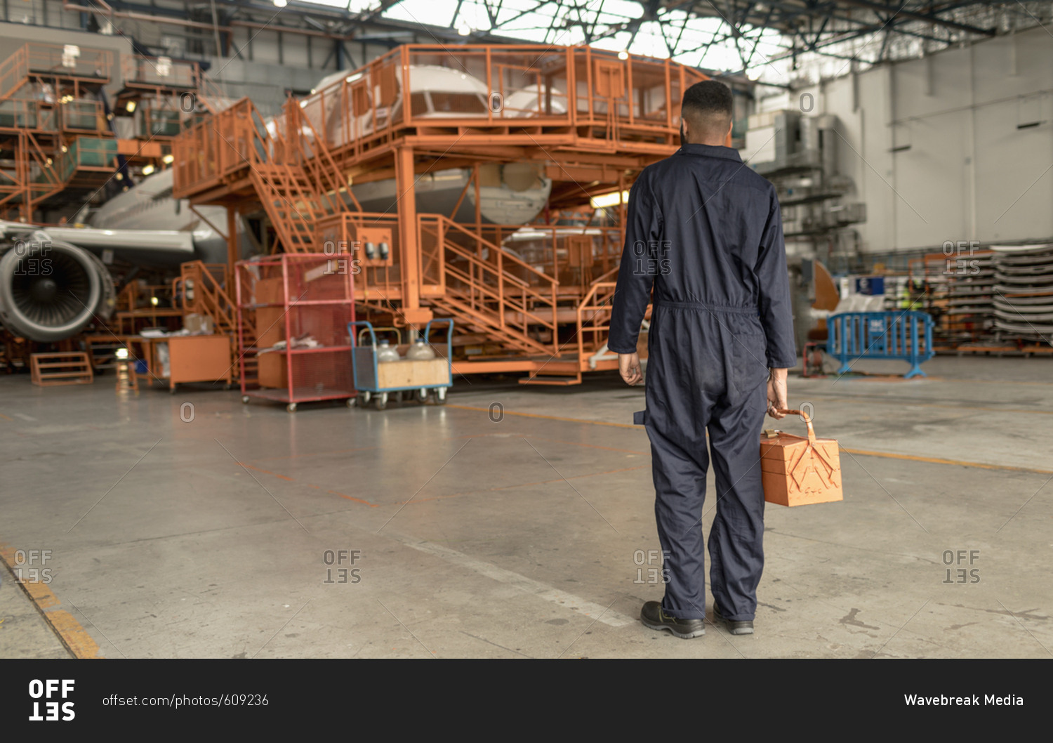 Rear view of male aircraft maintenance engineer holding tool kit at airlines maintenance facility