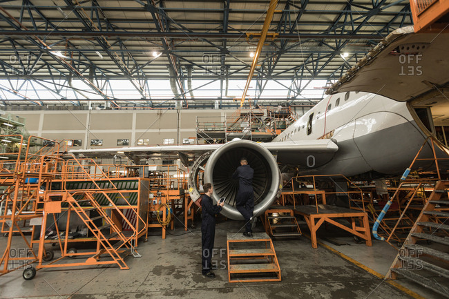 Aircraft maintenance engineers examining turbine engine of aircraft at airlines maintenance facility