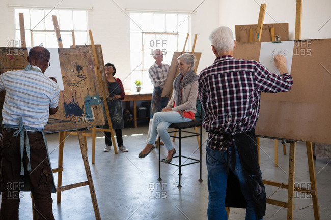 Woman sitting on chair while artist drawing on paper in art class