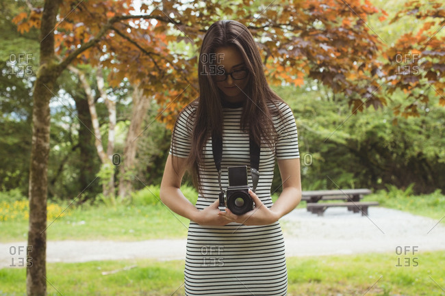 Woman looking clicked photos on vintage camera at forest