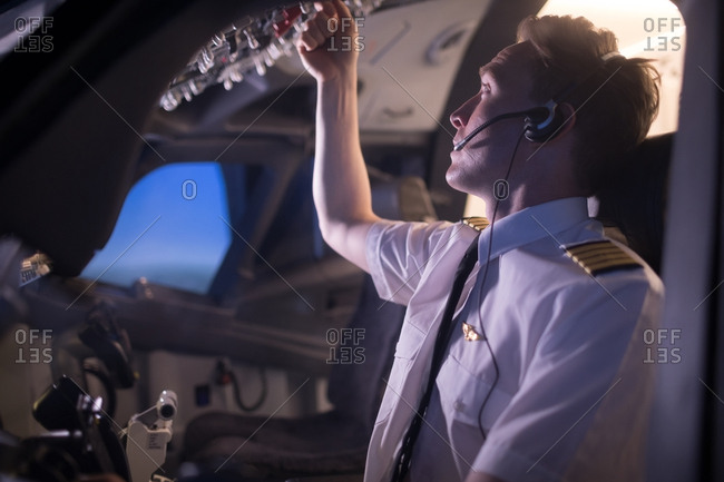 Young male pilot switching control in airplane cockpit seen from window