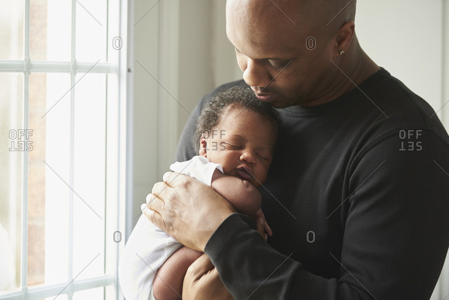 Black father carrying sleeping baby son near window