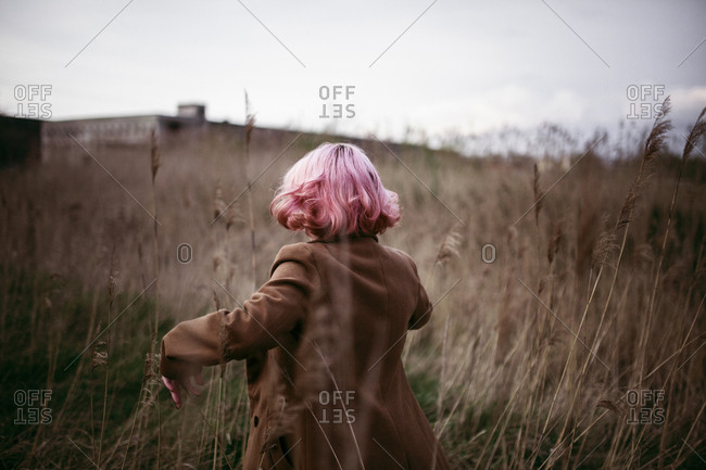 Caucasian woman with pink hair running in field