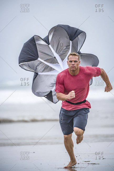 Man running on beach with parachute strapped to his waist