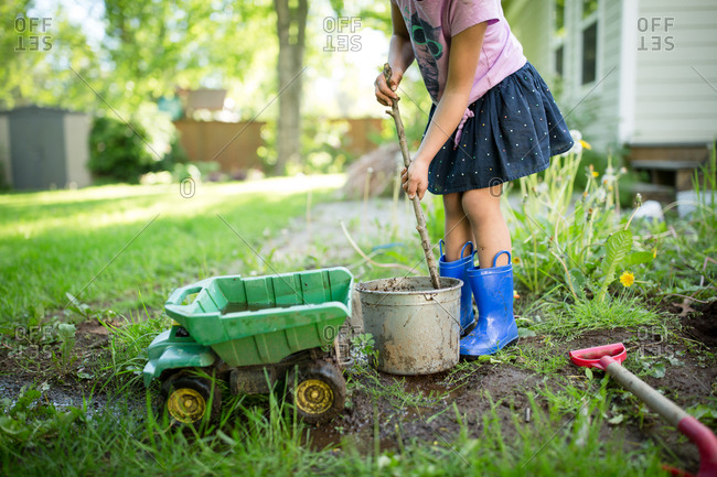Girl stirring bucket of dirt with a stick