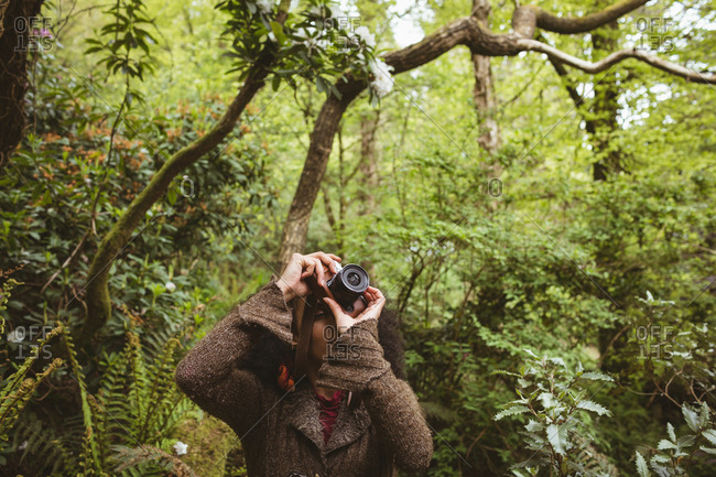 Woman photographing from camera against trees at forest