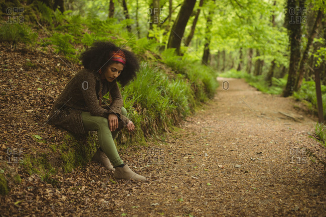 Full length of young woman relaxing by dirt road at forest