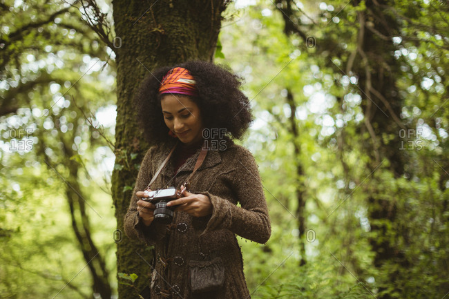 Young woman with camera by tree standing at forest