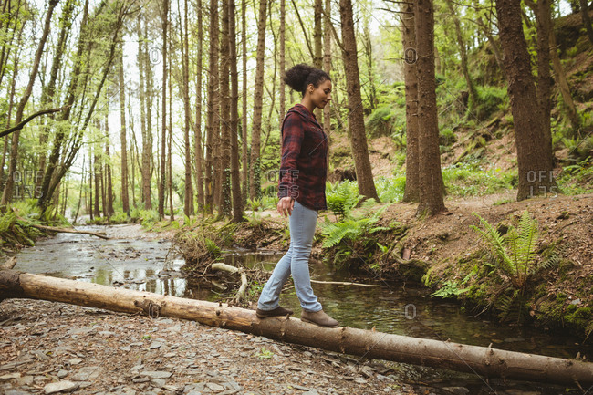 Full length of young woman walking on fallen tree at forest