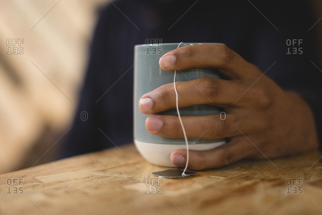 Cropped hand of young man holding tea cup while sitting at table in cafe