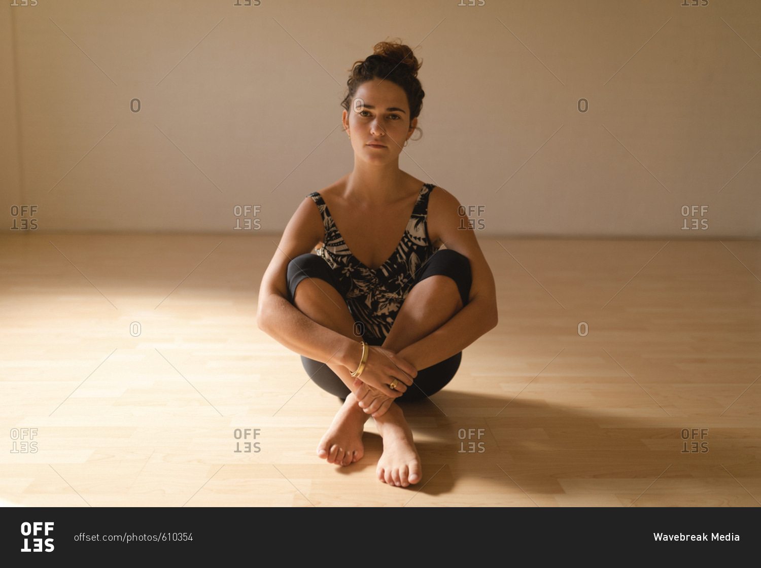 Portrait of young woman hugging knees while sitting on floor at yoga studio