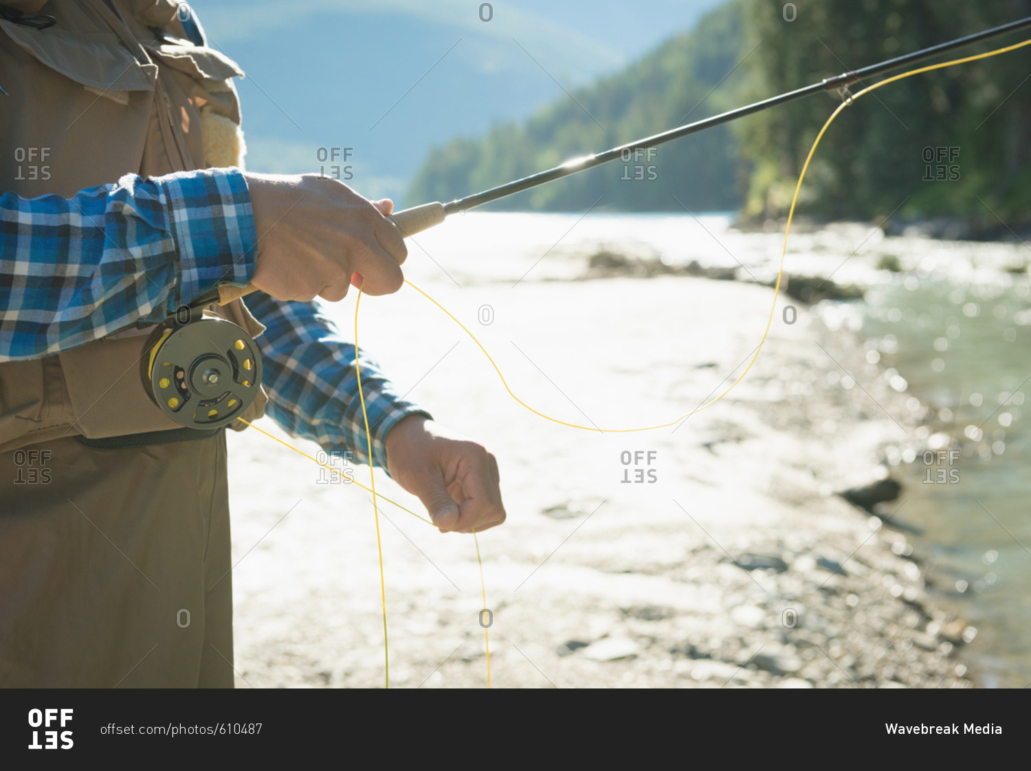 Mid section of man holding yellow thread while fishing in river against sky during sunny day