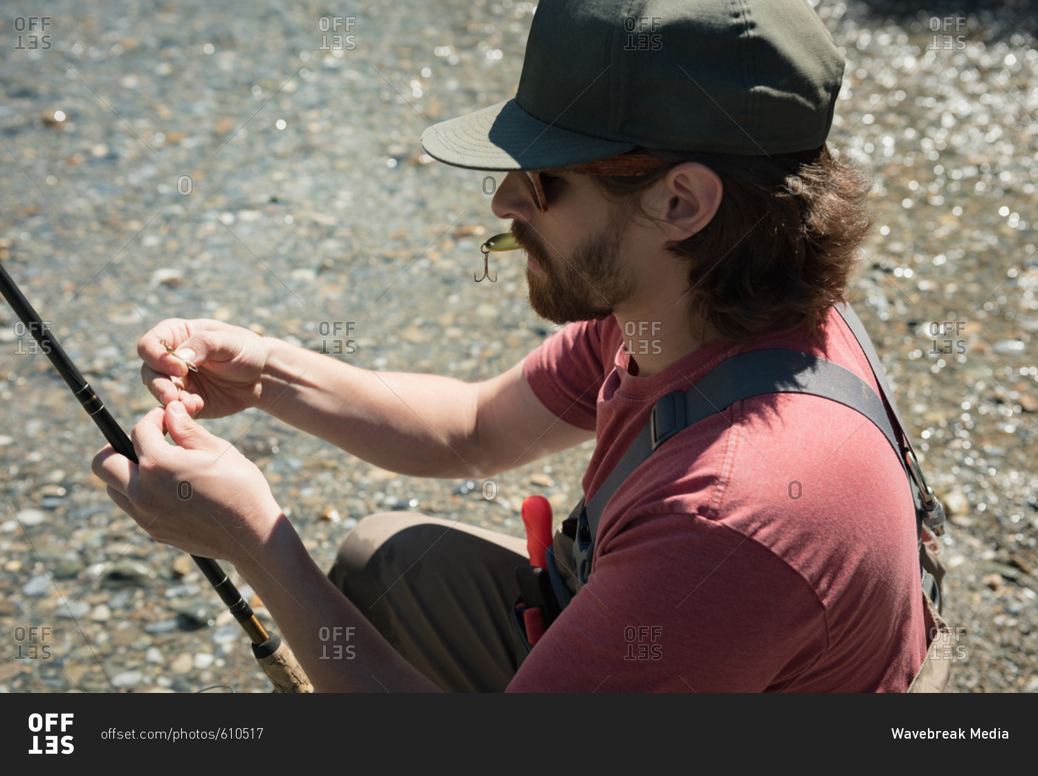 High angle view of man holding fishing hook and rod while crouching at riverbank