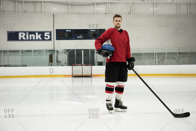 Portrait of male ice hockey player holding helmet and stick at rink