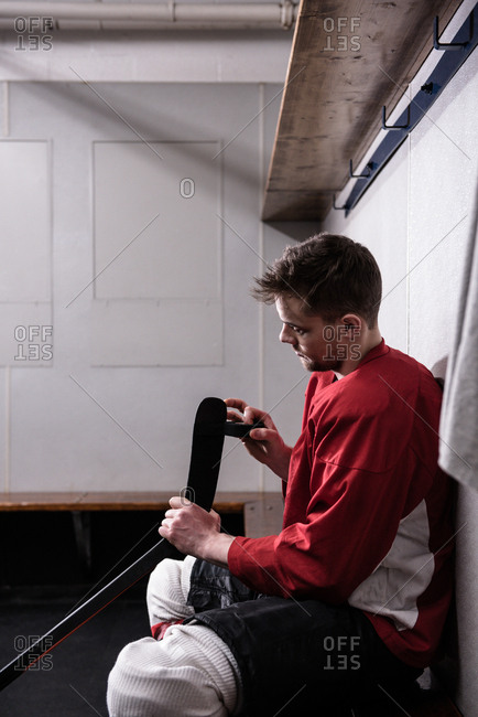 Side view of male player taping ice hockey stick in dressing room