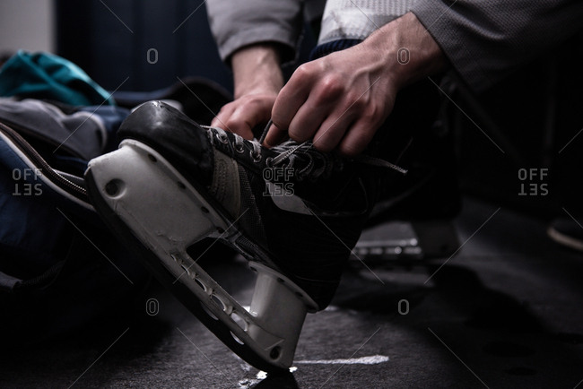 Low section of male ice hockey player tying skate in dressing room