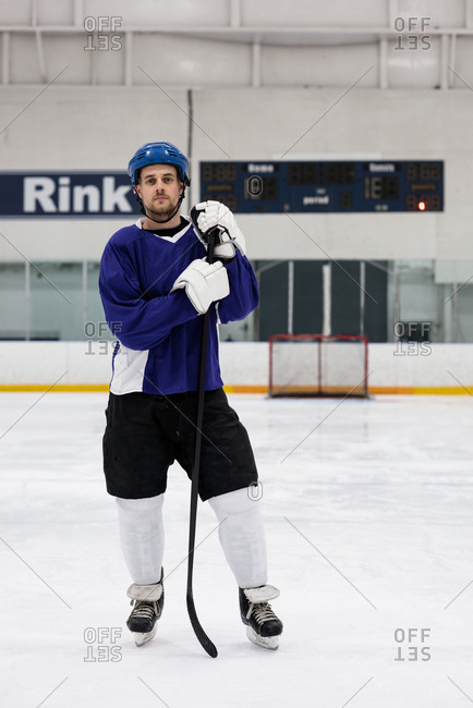 Full length portrait of male ice hockey player holding stick at rink