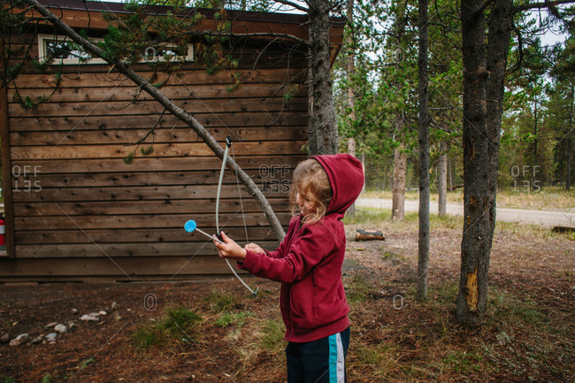 Boy with toy bow and arrow by cabin