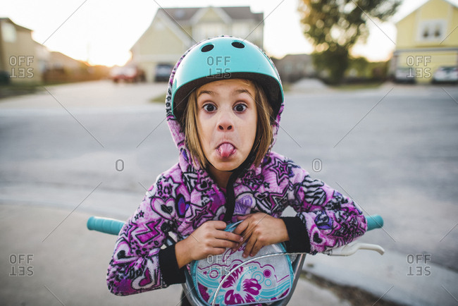 Portrait of playful girl sticking out tongue while riding push scooter on footpath