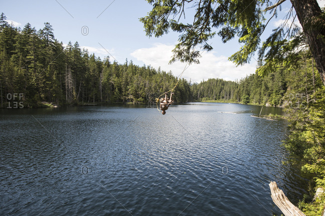 Carefree Man Jumping Form Rope Swing Into Lake Stock Photo