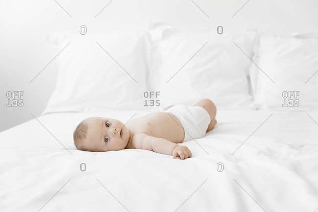 Baby boy lying on his back on a bed turning his head and looking at camera