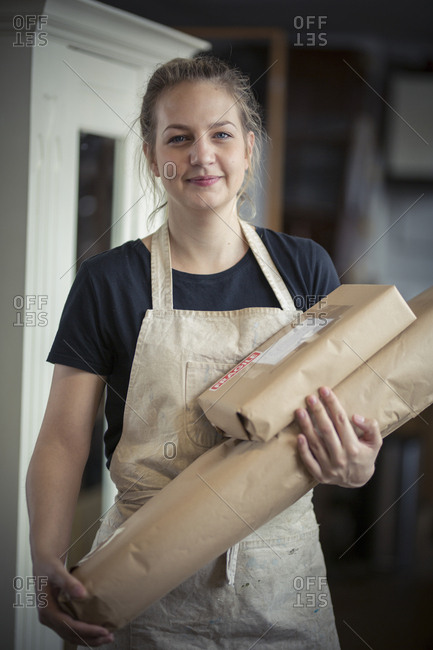 A young woman in a workshop, holding two packages wrapped in brown packaging paper, ready for dispatch