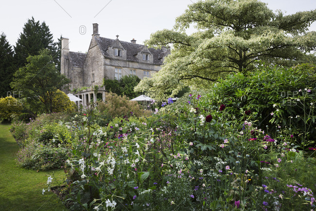 Exterior view of a 17th century country house from a garden with flower beds, shrubs and trees