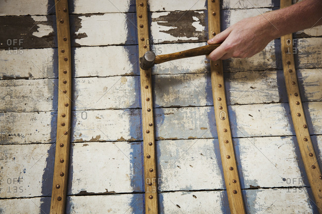 Close up of person in a boat-builder\'s workshop, working on a wooden boat hull