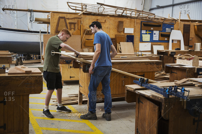Two men standing at a workbench in a boat-builder\'s workshop, working on piece of wood