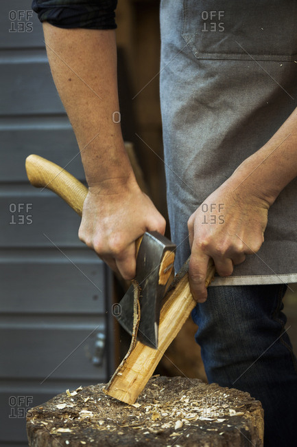 A craftsman holding a small axe, cutting down a small piece of wood on splitting block covered in wood shavings