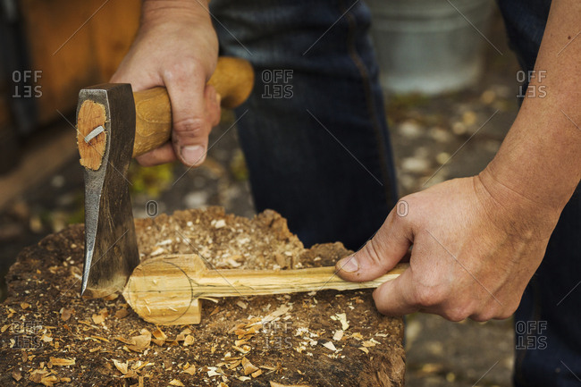 Close up of person holding a hand axe, cutting and shaping a small piece of wood on a splitting block covered in wood shavings