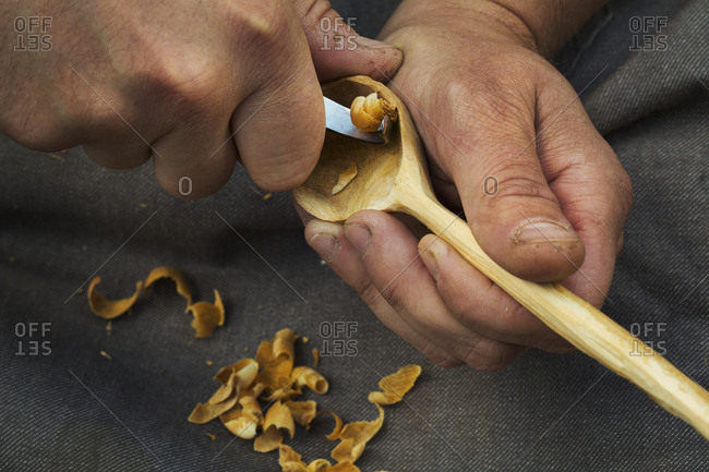 A craftsman carving wood, shaping the bowl of a hand carved wooden spoon with a sharp handheld tool