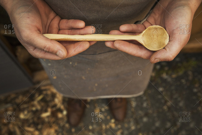 A man's hands holding a hand carved wooden spoon with a long tapering handle and smooth round bowl end